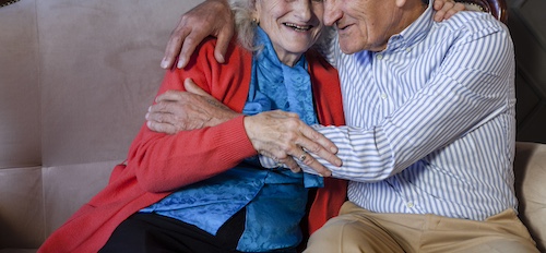 Couple de personnes âgées souriantes et complices dans leur canapé — rester à domicile grâce à l'AGMAD à Garches