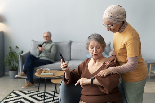 Une aide à domicile AGMAD aide sa cliente pour paramétrer sa montre connectée.
