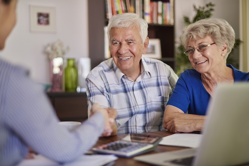 Couple de seniors souriants lors d'une consultation pour l'APA avec un conseiller — aide à domicile AGMAD Garches